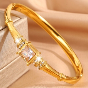 Detailed close-up of a golden bangle featuring a square clear stone and textured step design