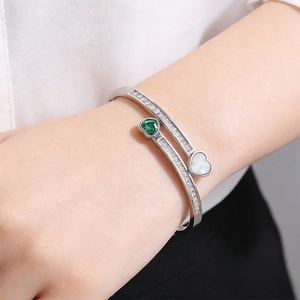 Detail of silver heart bangle with green zircon and mother of pearl on a woman's wrist