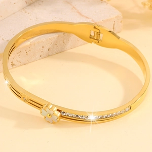 Détail du bracelet trèfle doré avec décor floral blanc et cristaux scintillants
