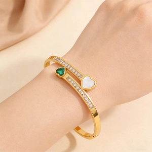 Close-up of golden open cuff bracelet featuring emerald heart stone and pave cubic zirconia