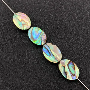 Macro shot of oval natural abalone shell beads showing colorful iridescent luster on a metal probe