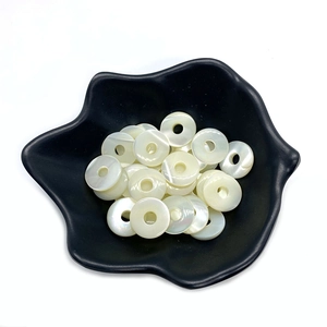 Flache runde weiße Perlmuttmuschelperlen für DIY-Schmuck auf einem schwarzen Teller