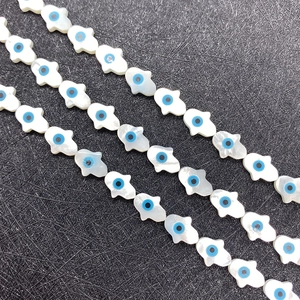 Macro view of white mother of pearl Hamsa Hand beads with blue evil eye for DIY jewelry