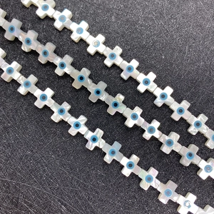 Detailed view of white shell cross beads with blue evil eye pattern for jewelry making