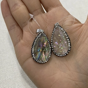 Detail of abalone shell teardrop pendants with pavé crystals held in a hand