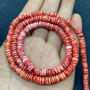 Close-up of hand holding 5-8mm dyed shell disc beads in vibrant orange and red colors