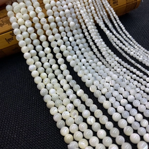 Macro shot of white natural shell round beads in multiple sizes on black textured fabric