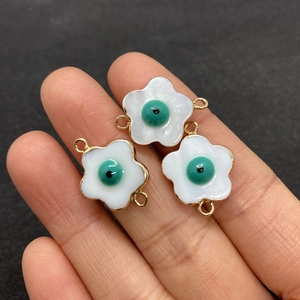 Detailed view of three white shell flower pendants with evil eye motifs and gold connectors