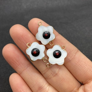 Three five-petal shell flower connectors for DIY necklaces held by hand for size reference