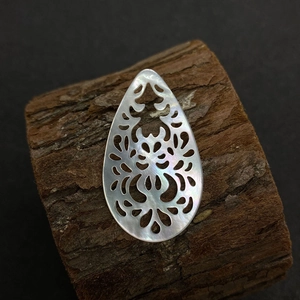 Vue macro d'un pendentif en forme de goutte ajouré sculpté en nacre naturelle