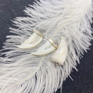 Three natural white mother of pearl horn pendants with silver caps on a soft feather background