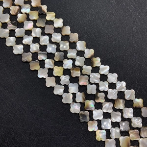 Perles trèfle en nacre naturelle polie avec éclat iridescent sur un fond noir texturé
