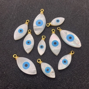 Flat lay detail of eleven evil eye shell pendants with golden bails on a black mat