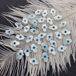 Cuentas de concha Mano de Fátima con diseño de ojo turco sobre fondo de plumas blancas