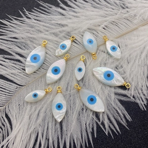 Handcrafted evil eye shell pendants with gold loops on an elegant white feather