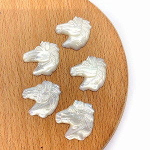 Detail shot of five carved horse head charms made of natural white mother of pearl shell