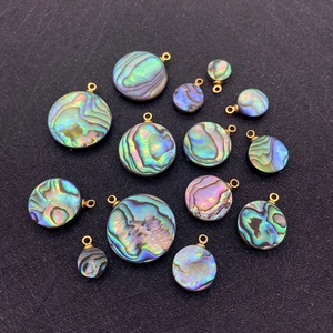Pendentifs ronds en nacre d'abalone naturelle avec anneaux dorés sur fond noir texturé