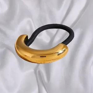 Minimalist black elastic hair tie with a polished gold crescent metal cuff on white satin