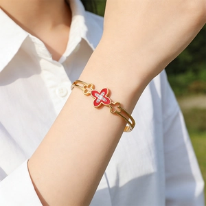 Detailed view of gold open bangle with red clover motif and sparkling crystal accents