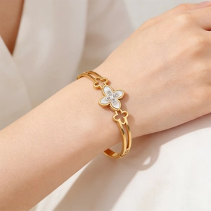 Macro detail of a gold hollow clover bracelet featuring a white shell inlay and crystals