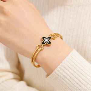Detail of gold clover bangle with black enamel and diamonds on a model's wrist