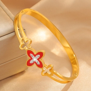 Macro view of gold stainless steel bangle featuring red clover and crystal details