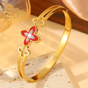 Elegant gold clover bangle with red enamel and pavé crystals on a marble background
