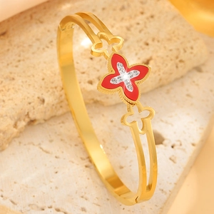 Detailed macro of gold clover bracelet with red enamel and micro-set diamonds