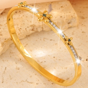 Detail view of gold floral bangle featuring emerald-green gems and cubic zirconia stones