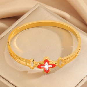 Detail view of gold clover bracelet with red inlay and crystals on silk background