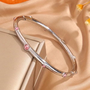 Detalle de pulsera plateada estilo bambú con cristales rosas sobre seda champán