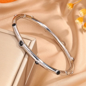 Primer plano de brazalete plateado minimalista con gemas negras sobre fondo de satén dorado