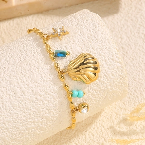 Détail d'un bracelet coquillage doré avec breloque étoile et perles sur fond sable