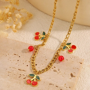 Dettaglio della collana dorata con ciliegie rosse e perline su superficie in pietra