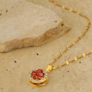 Detailed close-up of golden clover pendant with red heart crystals on stone