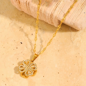 Golden clover pendant necklace with sparkling crystals on natural stone background