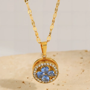 Detailed shot of spinning gold clover necklace with blue crystals on a stone pedestal