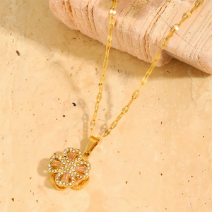 Close-up of golden clover necklace with pink gemstone and zircon on marble background