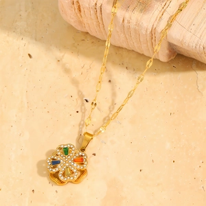 Detail of rotating gold clover necklace with multicolored zircon stones on stone surface