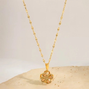 Elegant rotating four-leaf clover necklace with pink zirconia on warm beige pedestal