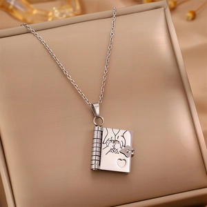 Macro shot of silver book locket pendant with engraved hands and heart on textured cushion