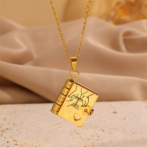 Golden book locket necklace with heart detail and fine chain on stone pedestal