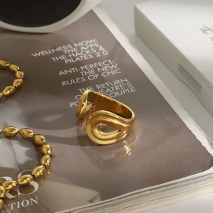 Anillo envolvente dorado de diseño artístico con ondas sobre una revista de moda