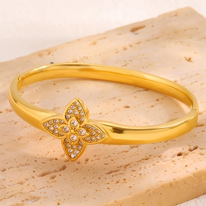 Close-up of gold-plated clover bangle featuring micro-pave crystals on stone background