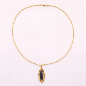 Detalle de collar de cadena dorada con colgante de obsidiana negra y marco dorado tallado fino