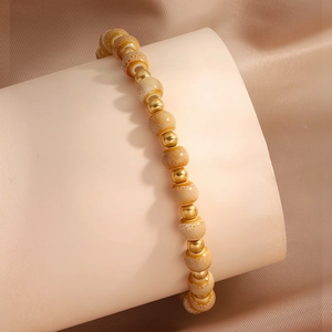 Nahaufnahme von goldenen Metallperlen und orangefarbenen Keramikperlen an einem Armband