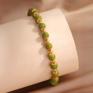 Detail eines handgefertigten Keramikperlen-Armbands mit grünen Mustern und Goldperlen