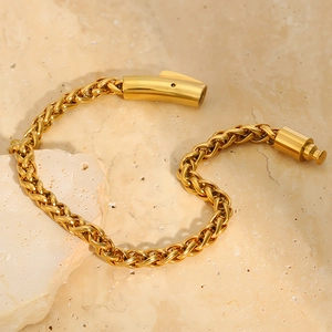Detail of golden wheat chain bracelet with cylindrical push-in clasp on stone background
