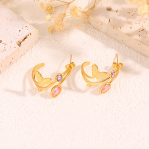 Gros plan de boucles d'oreilles papillon dorées avec pierres violettes et roses sur pierre