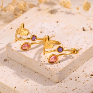 Détail des boucles d'oreilles papillon dorées avec cristaux violets et roses sur pierre
